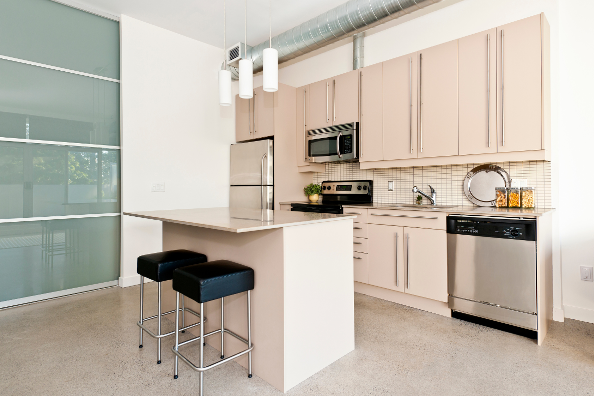 A modern kitchen with light-colored cabinets, a central island with bar stools, stainless steel appliances, and pendant lighting. The neutral tones create a clean and inviting atmosphere, showcasing the benefits of soft, calming paint colors in interior design.