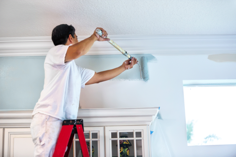 A painter uses a roller to apply light blue paint to a wall, focusing on the crown molding detail.