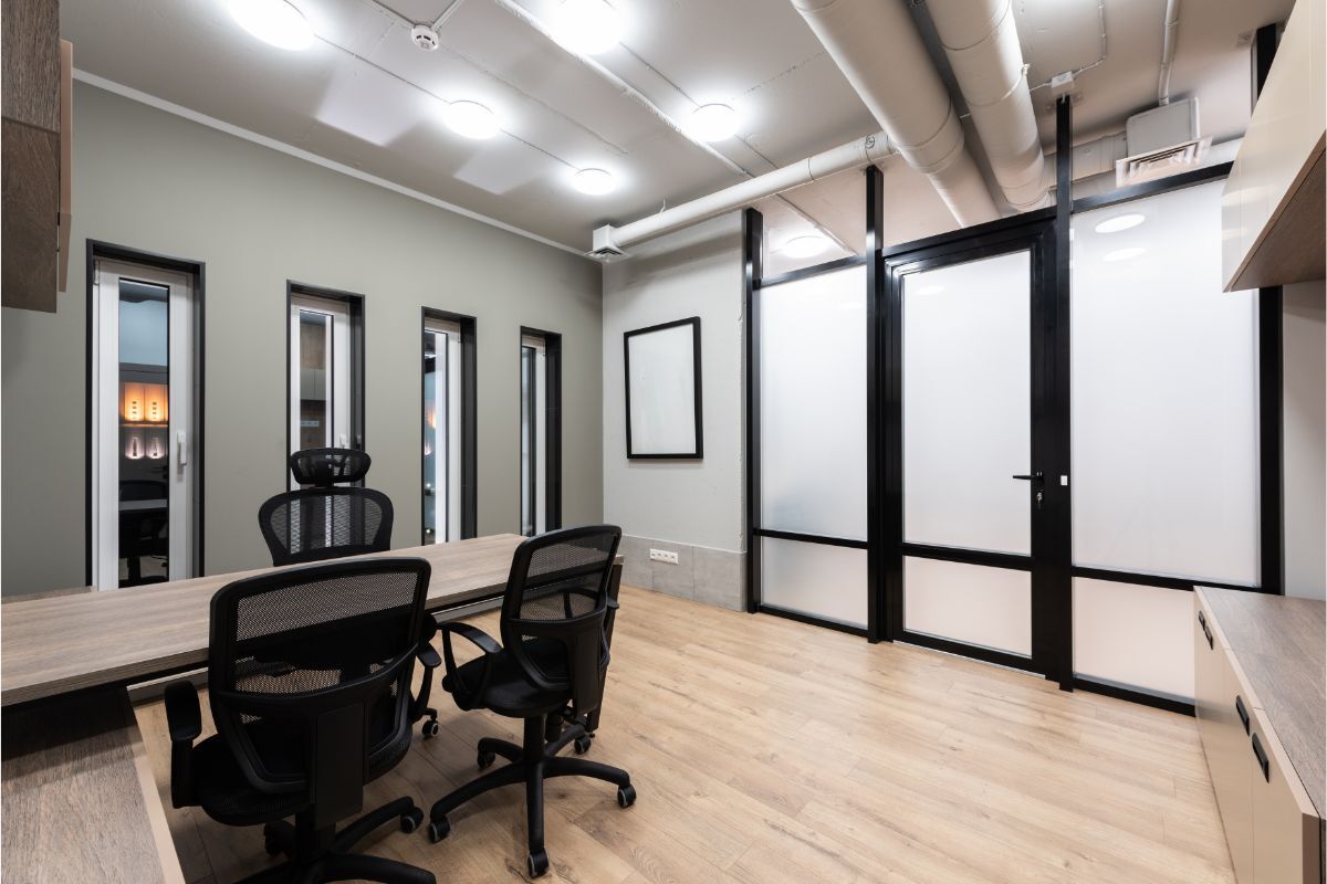 Modern office space with neutral walls, black accents, and a minimalist design featuring glass partitions, wooden flooring, and ergonomic chairs.