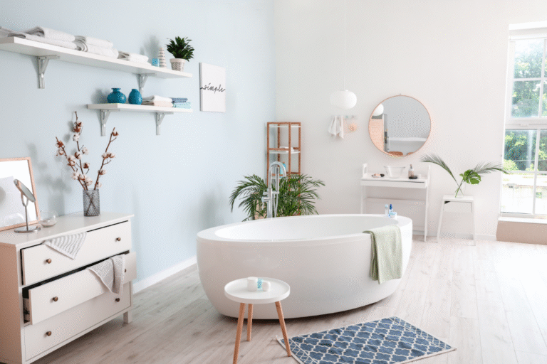 Modern bathroom with light blue walls, white fixtures, and minimalist decor including shelves, plants, and a freestanding bathtub.
